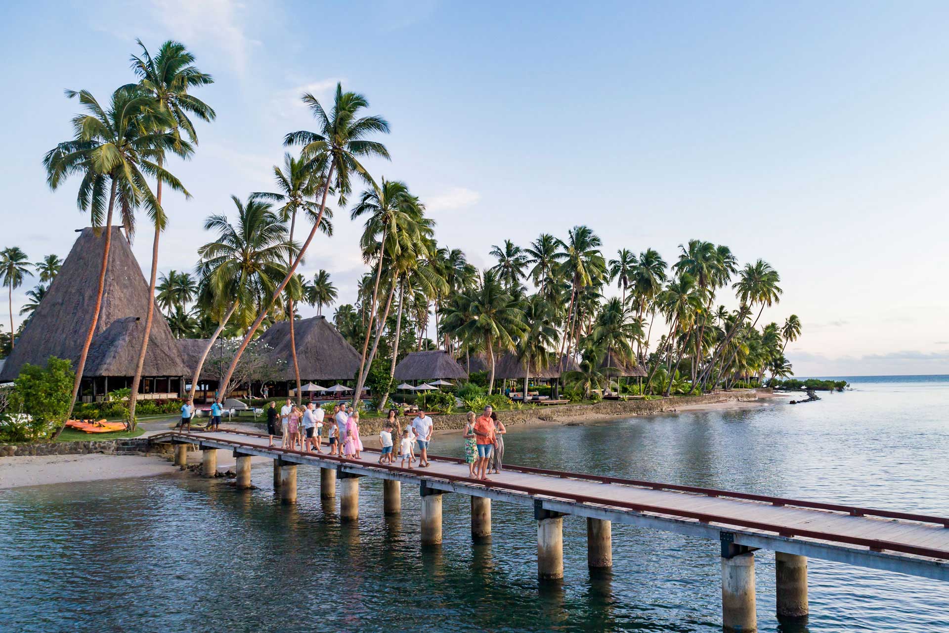 Image shows a multigenerational family walking down the jetty at sunset at Jean-Michel Cousteau Resort Fiji, an all-inclusive family resort in Fiji.